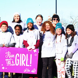 A group of Girls on the Run participants and volunteers with a sign at a 5k.